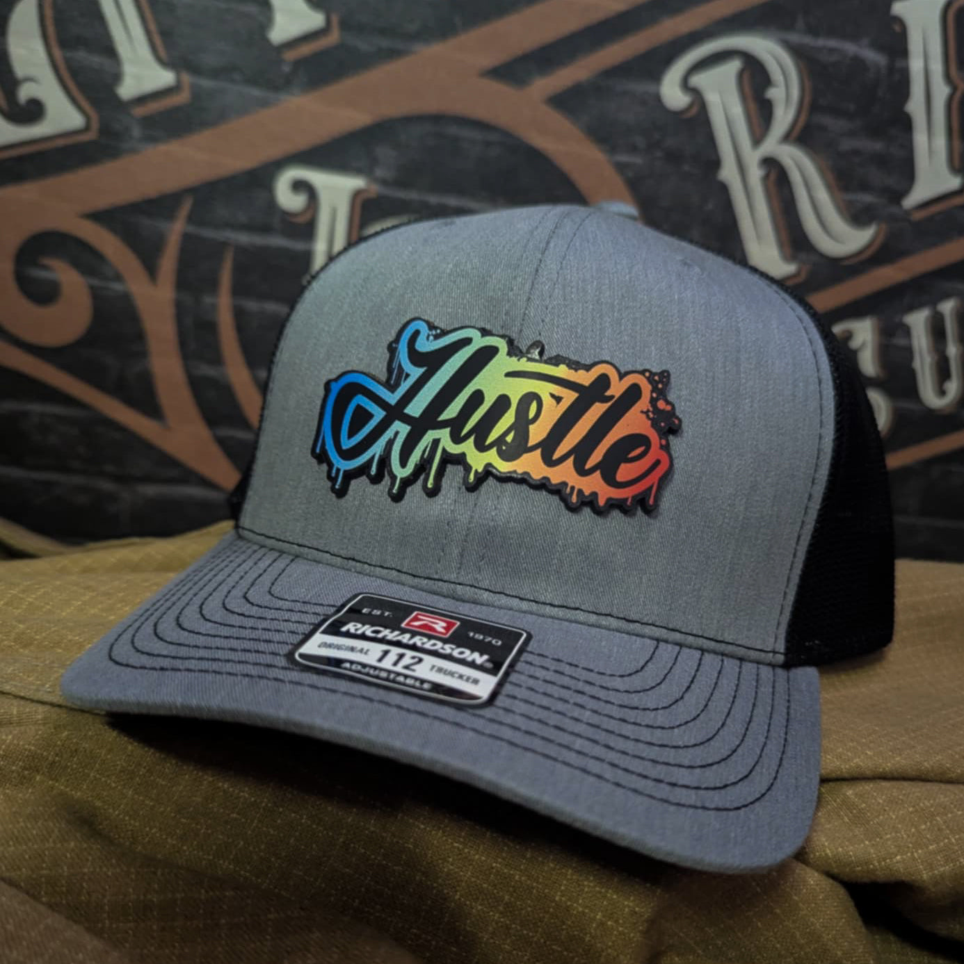 Richardson hat with real leather patch reading “Hustle” in rainbow gradient graffiti style on gray trucker hat
